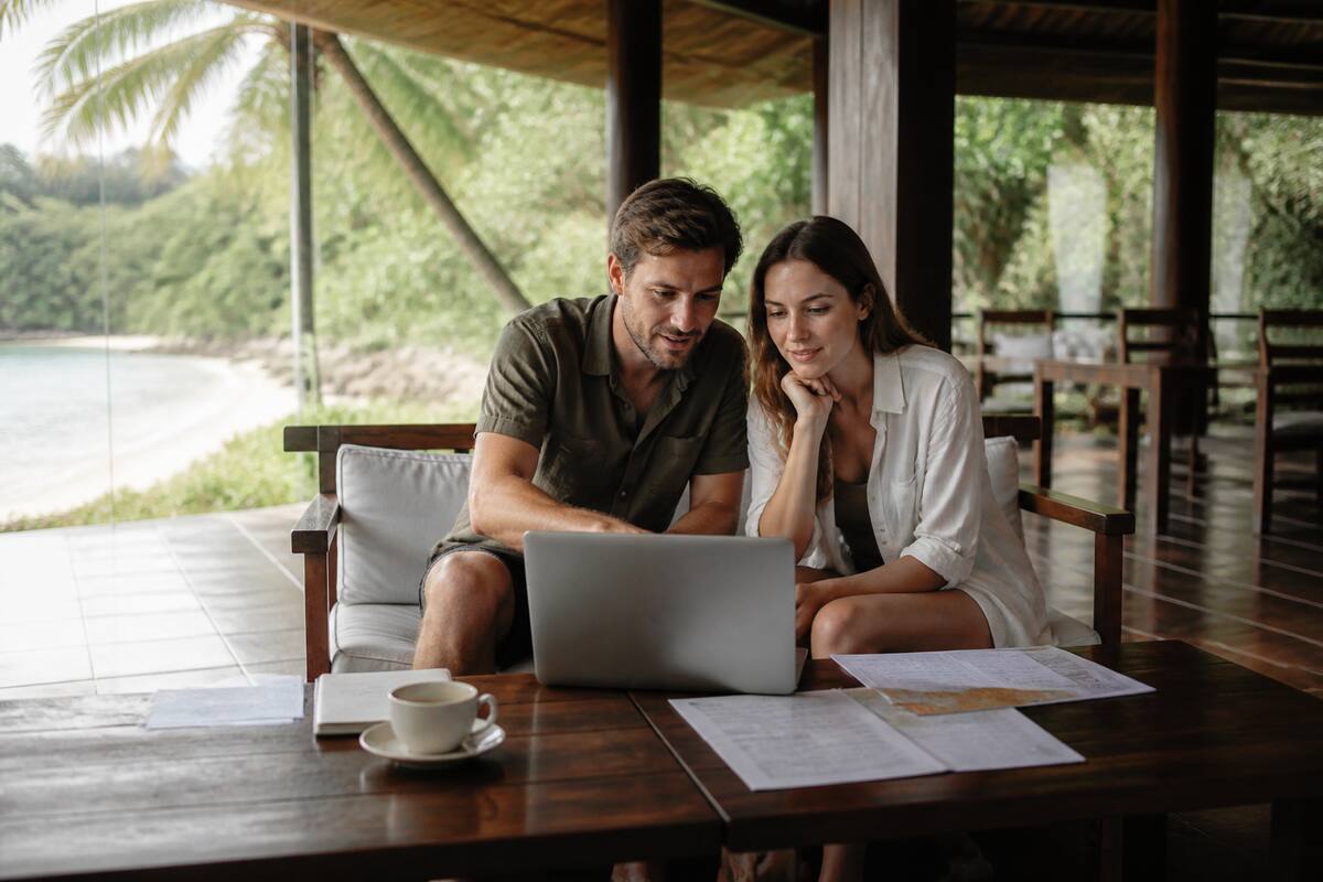 Koppel dat reisopties vergelijkt op een laptop met papieren op tafel, in een rustige vakantiesetting