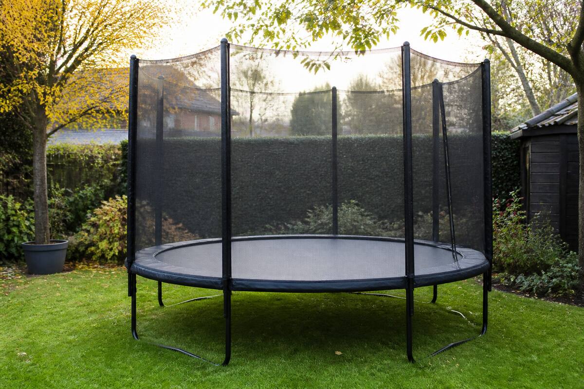 Trampoline in een tuin met veiligheidsnet en randkussen zichtbaar